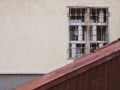 A yellow wall on which an old dirty window with a metal grill is obliquely closed with corrugated rusty iron