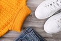 Yellow warm pullover for cold autumn, jeans denim and winter weather with white casual leather sneakers on wooden background