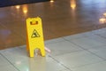 Yellow warning plate wit Caution wet floor icon on slippery tile floor st shopping mall indoors Royalty Free Stock Photo