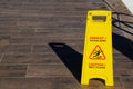 Yellow warning sign for wet floor standing on brown tiled floor. The inscription on yellow information plate caution slippery