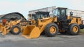 Yellow wheel loaders and graders stand in a row