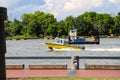 A yellow and white boat sailing through the vast green river water on the Savannah River with lush green trees and grass