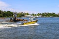 A yellow and white boat sailing through the vast green river water on the Savannah River with lush green trees and grass