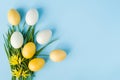 Yellow and white painted eggs on the green grass on a pastel blue background, Easter decor. Royalty Free Stock Photo