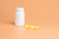 Yellow and white pills, tablets and white bottle on orange background Royalty Free Stock Photo