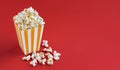 Yellow white striped carton bucket with tasty cheese popcorn, isolated on red background