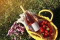 Yellow wicker bag with bottle of wine, strawberries, picnic blanket and beautiful flowers on green grass outdoors