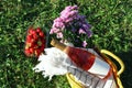Yellow wicker bag with bottle of wine, strawberries, picnic blanket and beautiful flowers on green grass outdoors