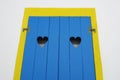 Yellow window frame and blue wooden door with two hollow heart shape gaps of a house front in Azores island