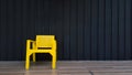 Yellow wooden chair put on brown tile floor with black shutter wall for background and copy space on right.