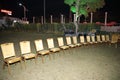 Yellow wooden chairs setup for a outdoor ceremony or event on grassland, beautiful decorated tree in background, night time shot