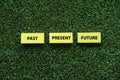A yellow wooden cube written with text of Past, Present and Future on a green grass background Royalty Free Stock Photo