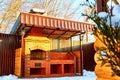 Yellow wooden gazebo with brick grill or barbecue in the yard on a Sunny winter day