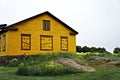 Yellow wooden house with closed shutters among green grass, yellow flowers and large stones Royalty Free Stock Photo