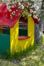 Yellow wooden playhouse with big window and red roof in the blooming garden with fresh green grass. White flowers petals Royalty Free Stock Photo