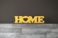 The yellow word Home made of wood stands on a wooden shelf against a gray wall.