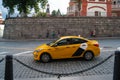 A yellow Yandex-Taxi car rides through the Moscow historic center along a stone-paved street. Antiquity, architecture, vintage