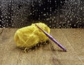 Yellow yarn with a purple crochet hook on a wooden table, seen through a window with rain drops