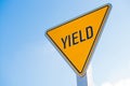 A yellow yield sign against a blue sky background Royalty Free Stock Photo