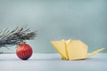 A yelluw paper mouse made using the origami technique looks at a pine branch with a red ball Royalty Free Stock Photo