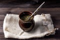 Yerba mate in ceramic matero with bombilla on linen bag on wooden table.