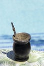 Yerba mate prepared to drink with its bombilla with a pool background out of focus on a table with a flower tablecloth. Yerba mate