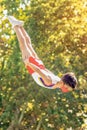 Yerevan, Armenia - October 19, 2019: Young boy athlete, gymnast in free fall in the air, over the ground. Green trees on backgroun