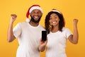 Yes. Excited black couple holding smartphones with empty screen shaking clenched fists, yellow background, mockup Royalty Free Stock Photo