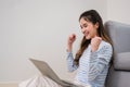 Yes! Happy excited young Asian woman sitting smiling and using laptop computer online with good news success in the living room at Royalty Free Stock Photo