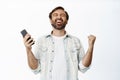 Yes. Happy man shouting with joy, winning on mobile phone, holding smartphone and celebrating, standing over white Royalty Free Stock Photo