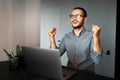 Yes. Portrait of young satisfied man working home at laptop, feels happy about victory and work done, wearing eyeglasses. Royalty Free Stock Photo