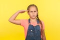 Yes sir! Portrait of responsible obedient little girl with braid in denim overalls saluting and looking at camera with respect Royalty Free Stock Photo