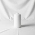 Ylindrical white pillar candle stands on a plain white fabric surface with a Royalty Free Stock Photo