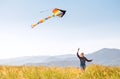 9YO Smiling girl with flying colorful kite running on the high grass meadow in the mountain fields. Happy childhood moments or Royalty Free Stock Photo