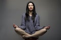 Yoga. Attractive girl, woman with long black hair sitting on stool and meditating, over a grey background. Royalty Free Stock Photo