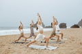 Yoga class on ocean shore. Group of young people doing warrior pose, meditating and exercising on the beach Royalty Free Stock Photo