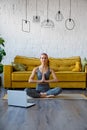 Yoga classes at home. A slender gray woman in a tracksuit is sitting in front of a laptop Royalty Free Stock Photo