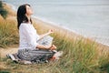 Yoga day. Stylish hipster girl sitting on beach in yoga pose and relaxing. Happy boho woman practicing yoga and meditation at sea Royalty Free Stock Photo