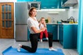 Yoga at home. A smiling young mother holding a baby in her hands and posing on a mat. Kitchen on the background. The concept of Royalty Free Stock Photo