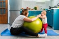 Yoga at home. A young mother leaning on a fit ball, funny communicates with her baby. The concept of fitness with children at home Royalty Free Stock Photo