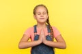 Yoga and inner harmony. Portrait of cute little girl with braid in denim overalls praying with closed eyes