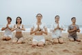 Yoga for inner peace. Group of young men and women meditating on the beach, practicing breathing yoga exercises Royalty Free Stock Photo