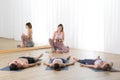Yoga instructor and group of young sporty people in yoga studio, lying and relaxing on yoga mats during restorative yoga