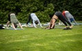 Yoga instructor and students outside on grass with yoga mats practicing downward facing dog pose