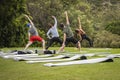 Yoga instructor and students outside on grass with yoga mats practicing poses