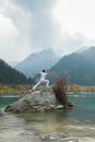 Yoga man in warrior pose on mountain lake rock, ourdoor activities concept