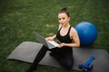 Yoga in the park with sunlight. A young girl in a lotus position sits on green grass holding a phone in her hand and watches Royalty Free Stock Photo