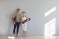 Yoga people. A man and a woman with yoga mats stand on a gray background in a bright classroom. Royalty Free Stock Photo