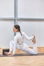 yoga stretch in vertical image of a Hispanic woman dressed completely in white. grabbing your foot with your hand on a mat