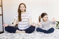 Yoga. Young woman and small daughter doing yoga lotus position in bed. relaxation and meditation at home in isolation Royalty Free Stock Photo